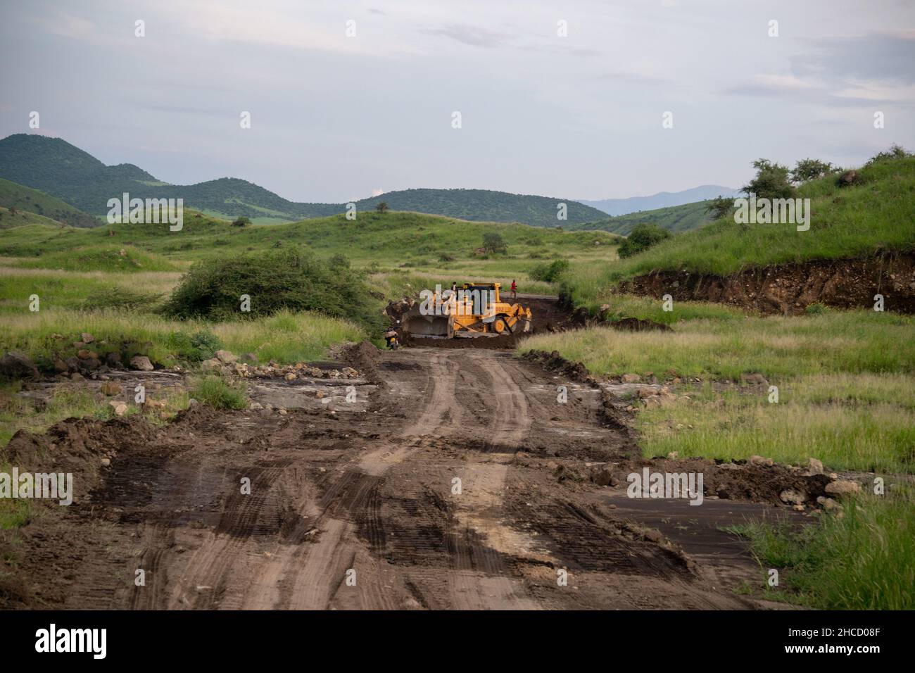 Excavator is Making Road in African Savannah. Group of African black men working for the construction of a road over an orange sandy off-road path Stock Photo