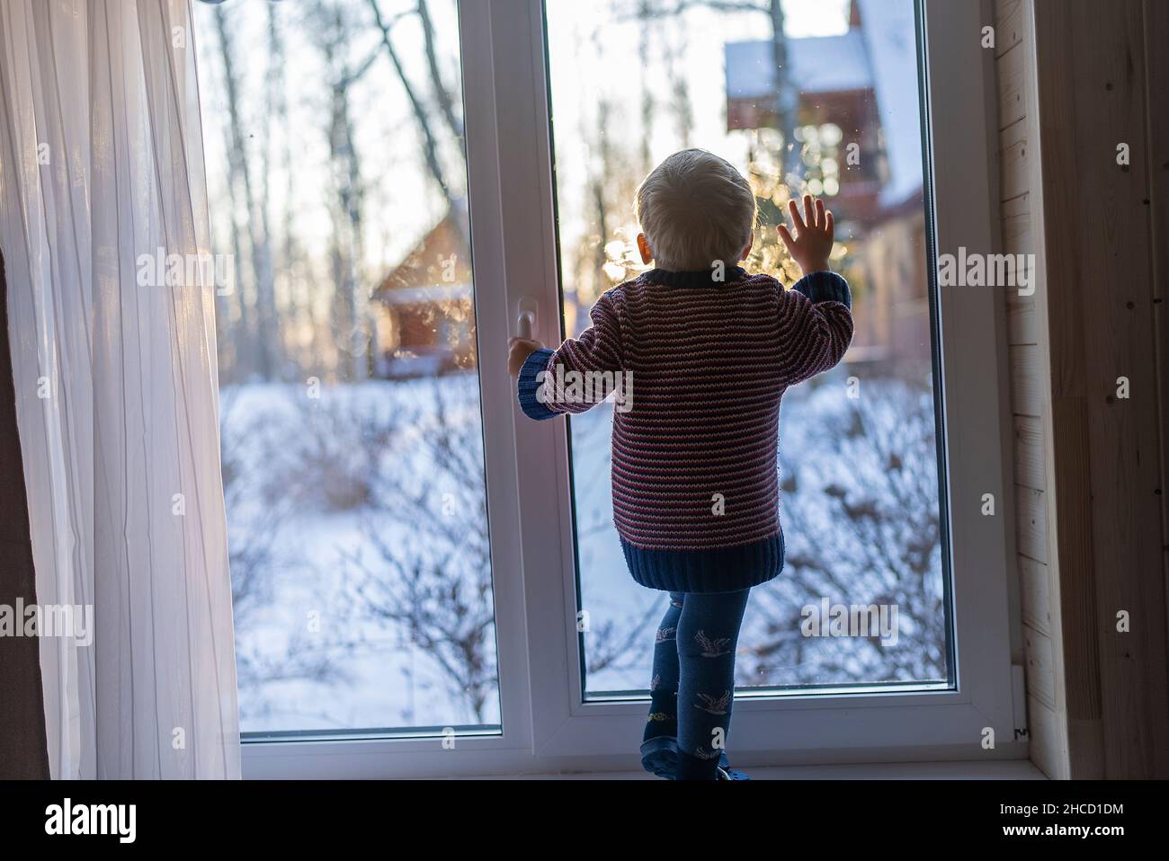 little boy stand near the window and look at the snowy street in winter, when it is very cold Stock Photo