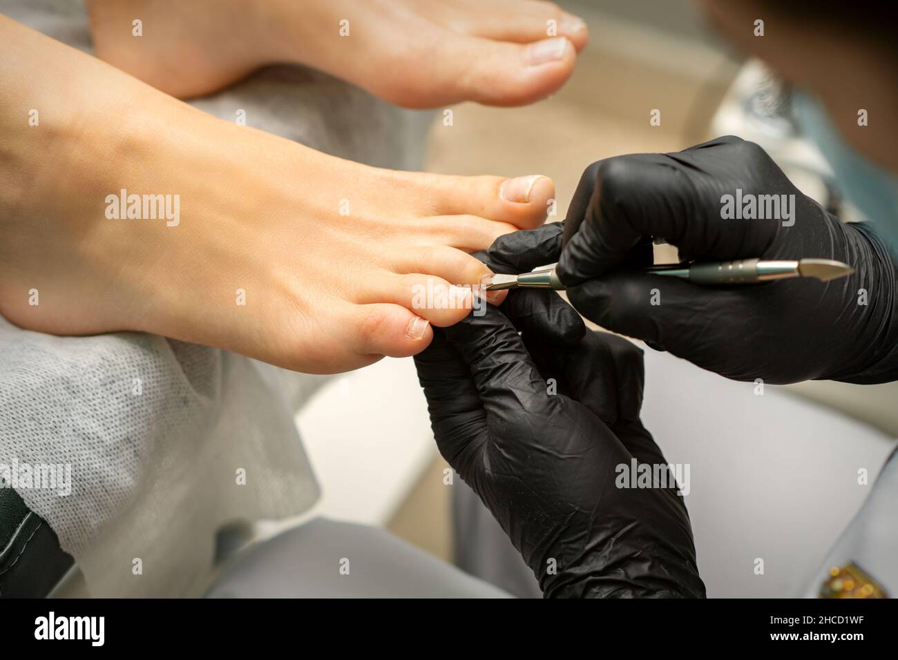 Cuticle Removal on Toes. Hands in black gloves of pedicure master