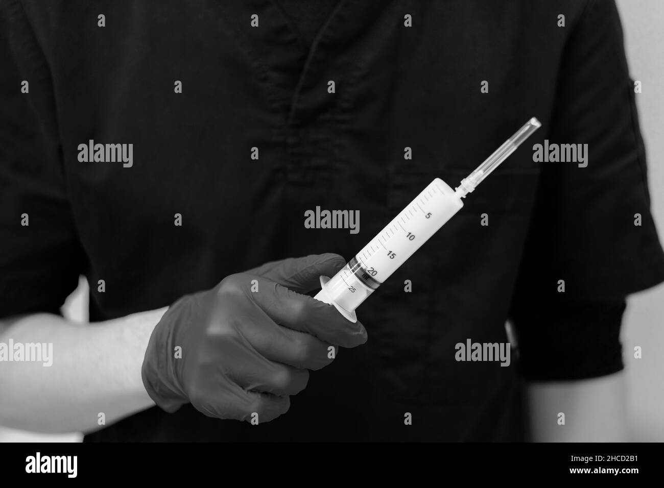 Large white syringe close-up in the hand of a doctor in a sterile glove. Selective focus. Black and white photo. Stock Photo