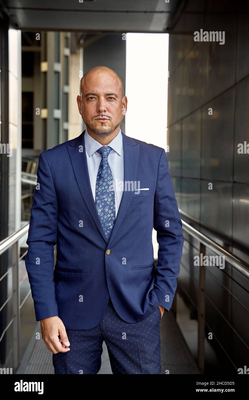 Confident bald male manager with hand in pocket looking at camera while standing outside contemporary building on street Stock Photo