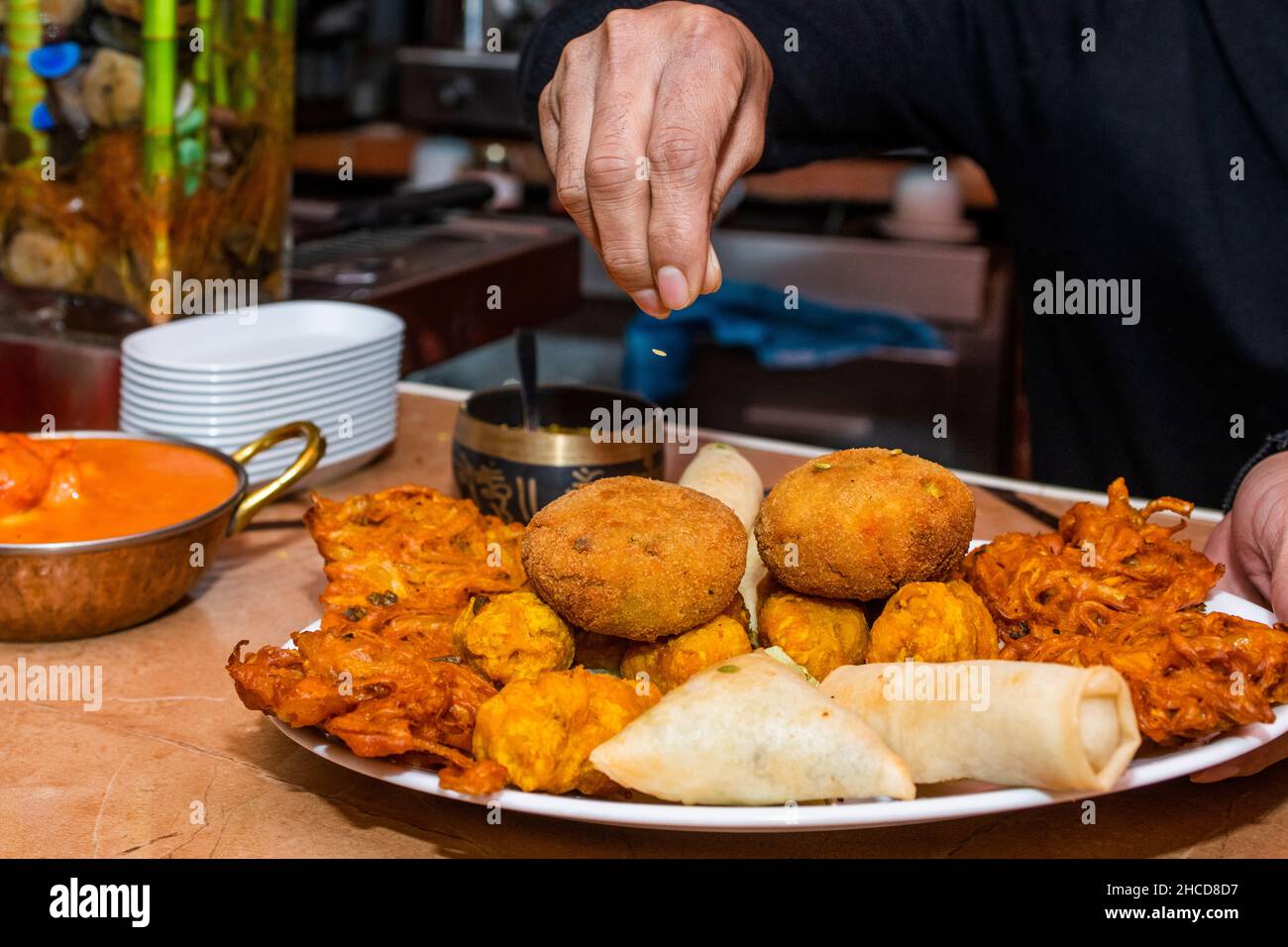Chef's hands seasoning a tray of assorted Hindu appetizers in a restaurant Stock Photo