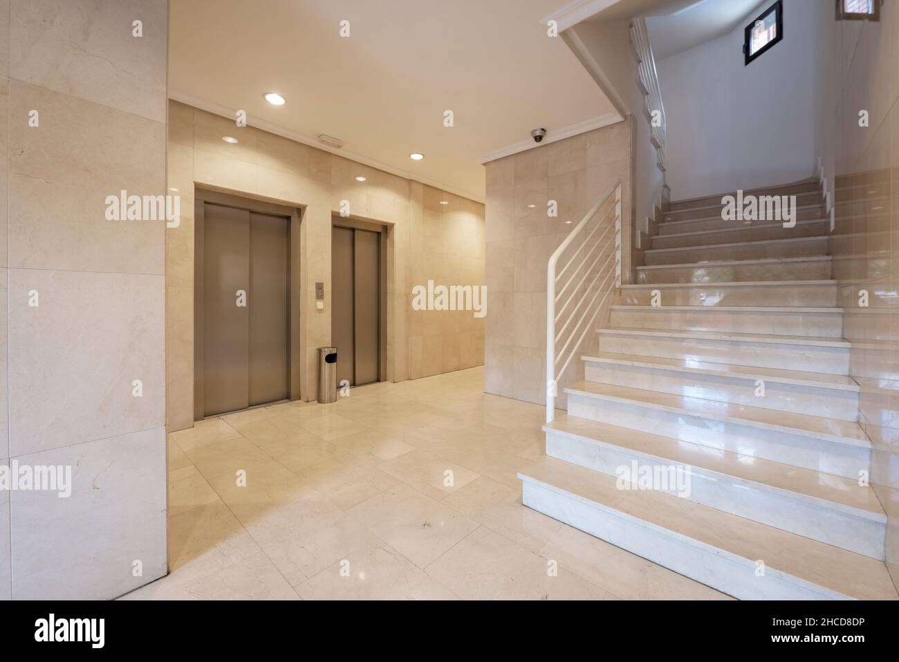 Entrance portal to a building with cream marble floors and walls, stairs and metal elevators Stock Photo