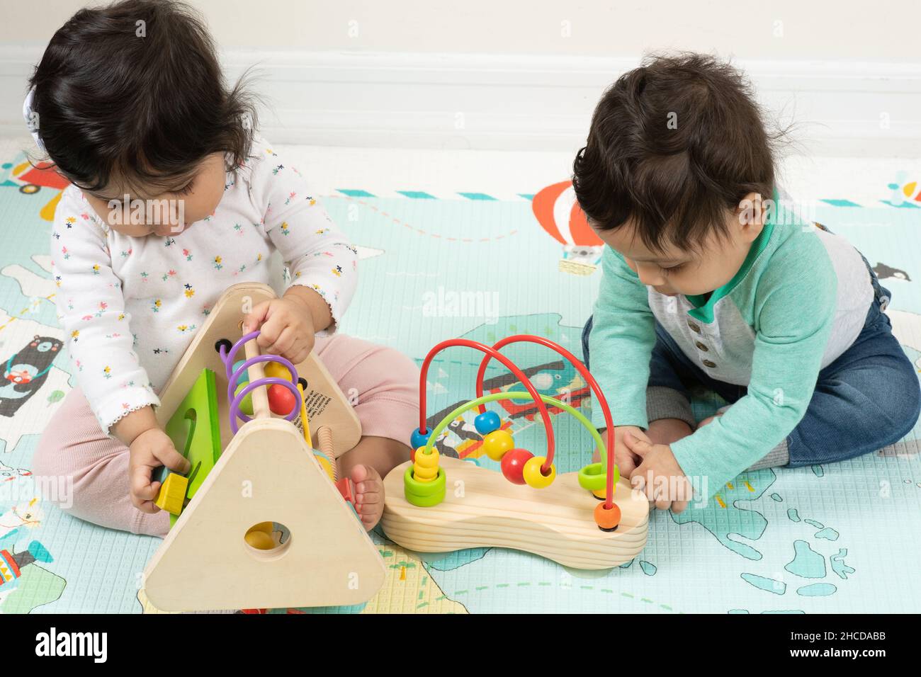 8 month old fraternal twin babies sitting near each other, both playing with toys Stock Photo