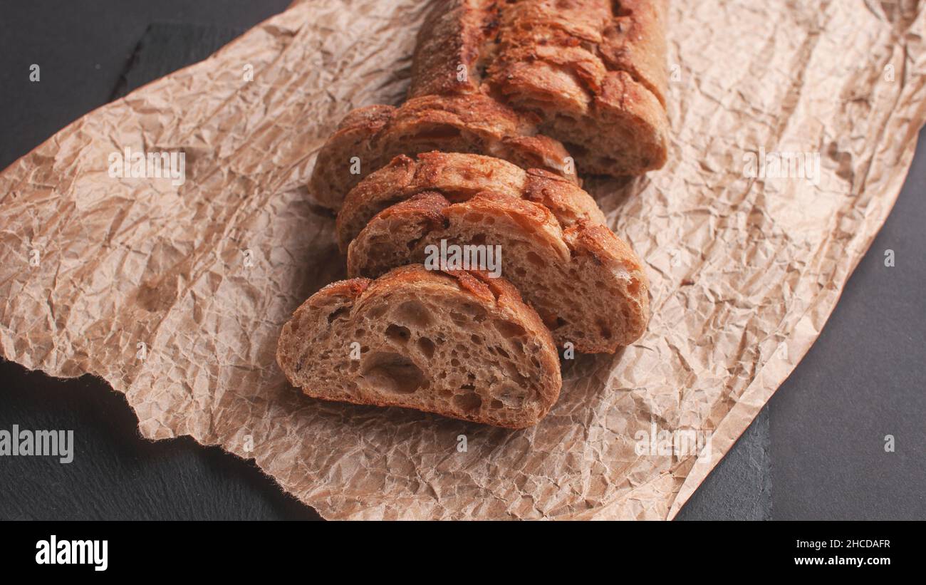 cereal baguette cut into pieces on parchment paper on black background Stock Photo