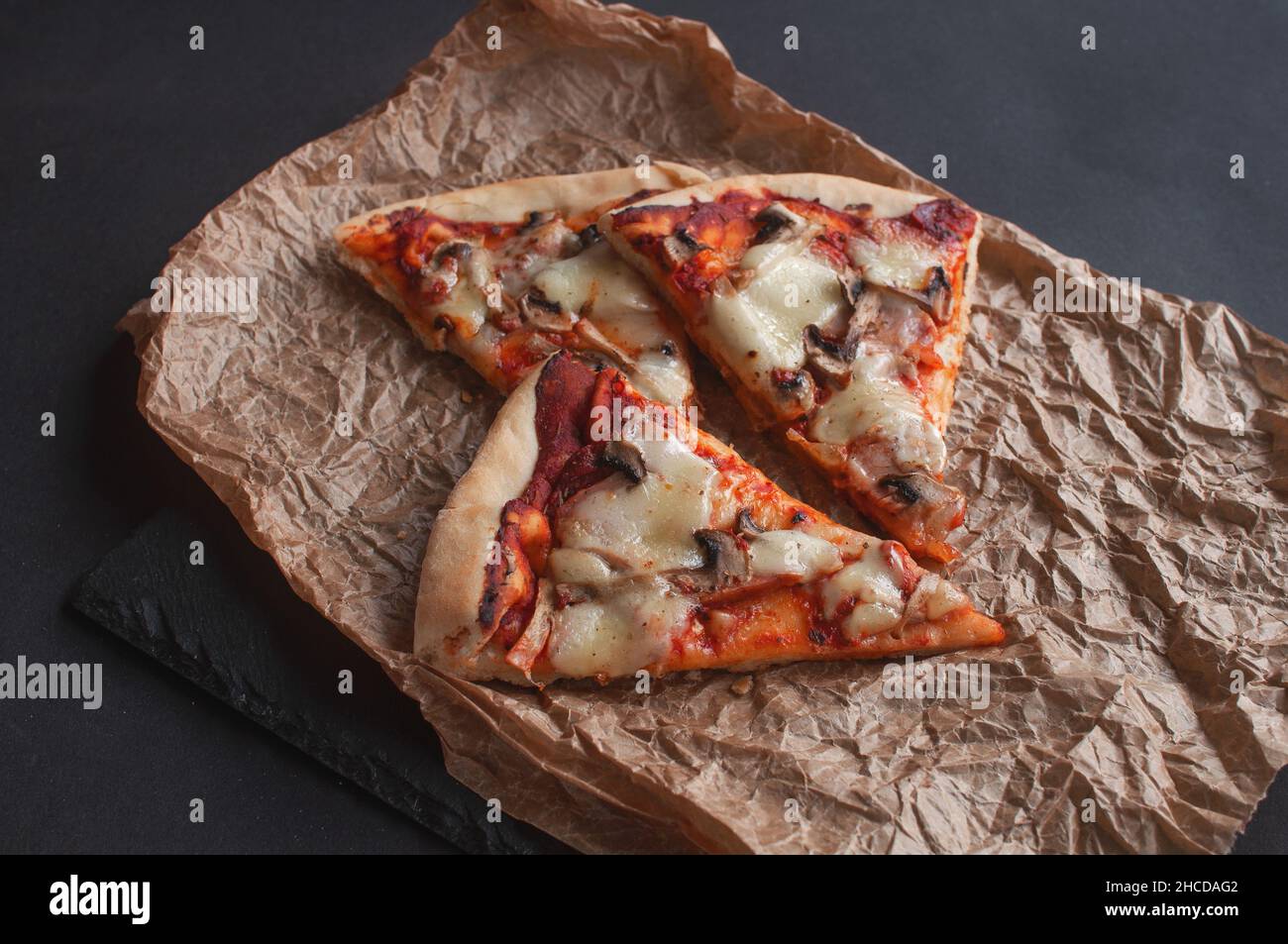 slices of freshly baked pizza on a black serving chalkboard on a dark background Stock Photo
