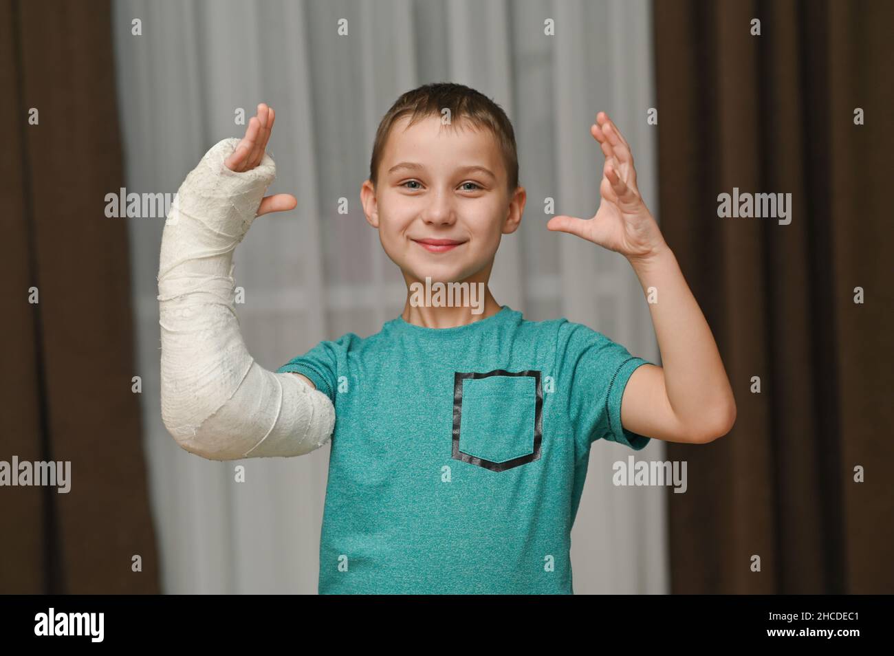 the boy raised two hands up. One arm is broken in a cast. Stock Photo