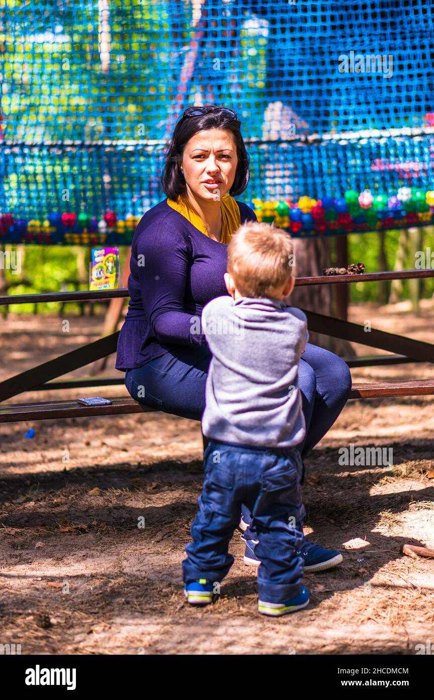 Woman sitting on a wooden bench next to a child in the Pyrlandia park. Stock Photo