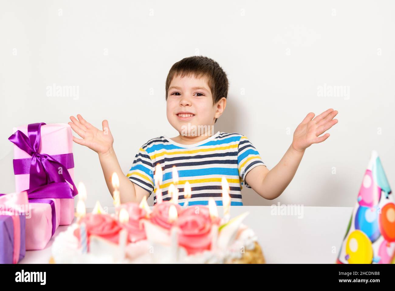 A handsome preschool boy with a cake on his birthday claps his hands on