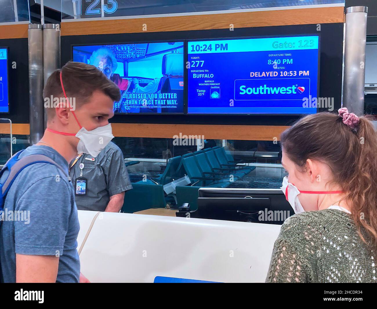 A couple wearing protective face masks are seen in front of a delayed flight sign at Orlando International Airport two days after Christmas. Due to flight crew shortages as a result of the COIVD-19 Omicron variant and due to other reasons, 760 flights to, from or within the US were canceled, and another 930 were delayed on December 27, 2021. Due to flight crew shortages as a result of the COIVD-19 Omicron variant and due to other reasons, 760 flights to, from or within the US were canceled and another 930 were delayed on December 27, 2021. Stock Photo