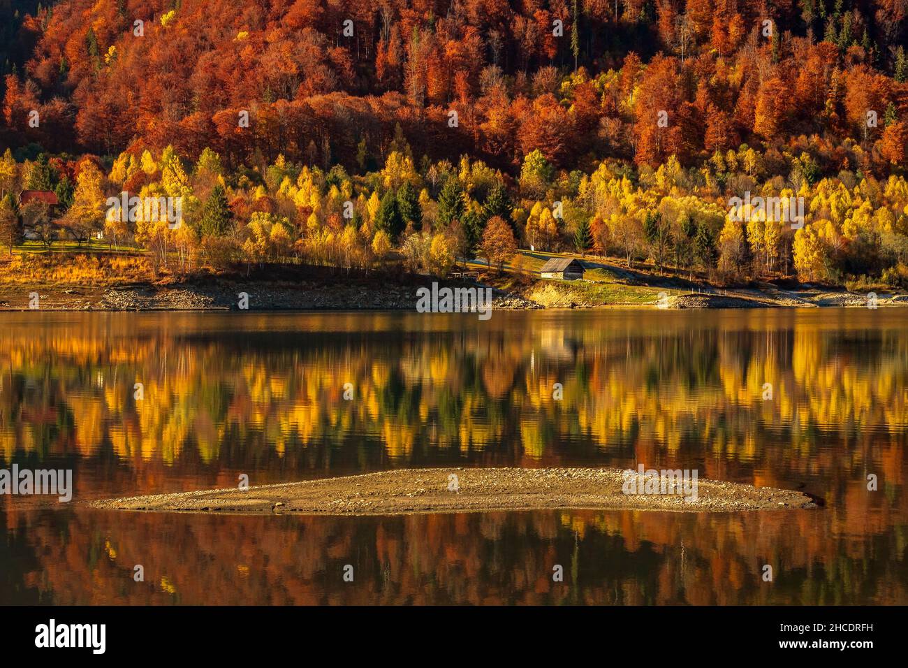 Small forest cottage on the Poiana Marului Lake shore reflected in a perfect symmetry. Photo taken on 31st of October 2021 in Poiana Marului reservati Stock Photo