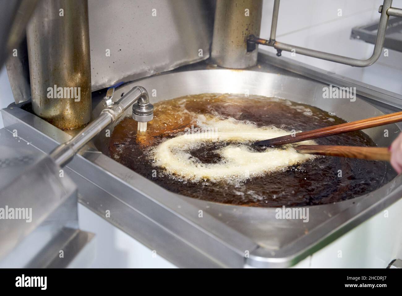From above the raw dough for churros or porras that is prepared in oil fried in a large stainless steel pan with wooden sticks in the professional kitchen. Typical Spanish breakfast Stock Photo