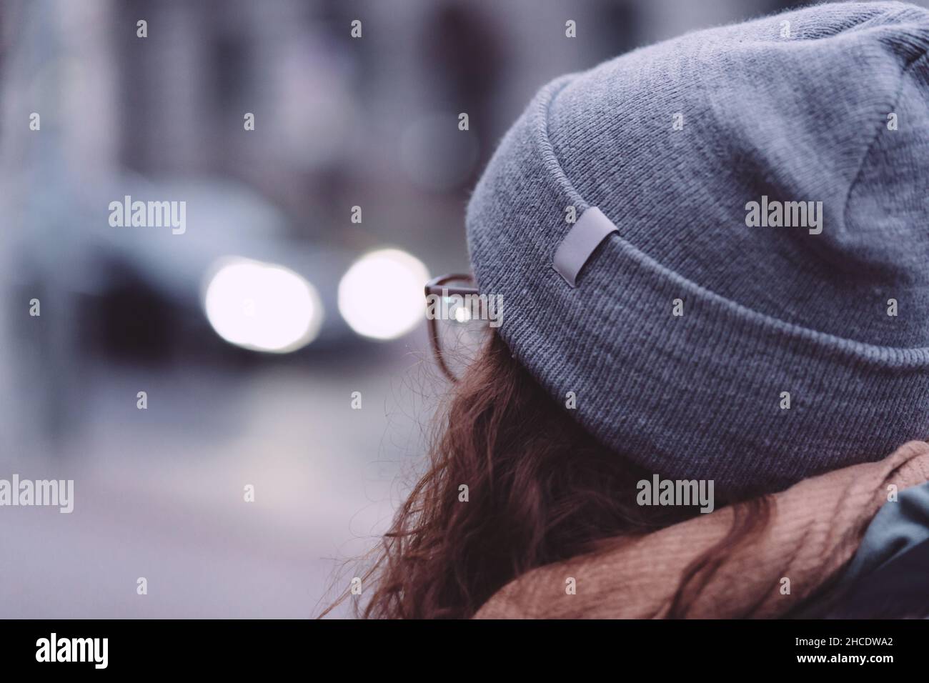 Rear view of a redhead lady wearing glasses, a hat, and a scarf outdoors Stock Photo
