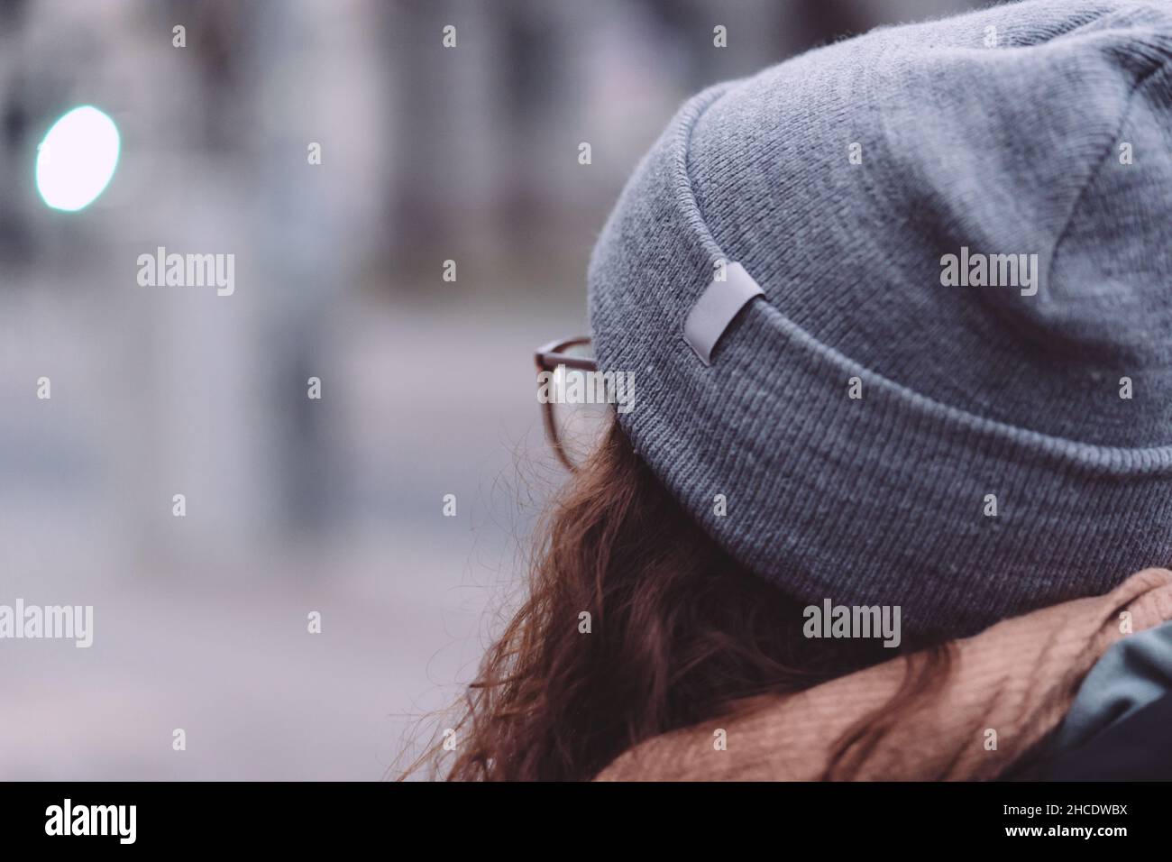 Rear view of a redhead lady wearing glasses, a hat, and a scarf outdoors Stock Photo