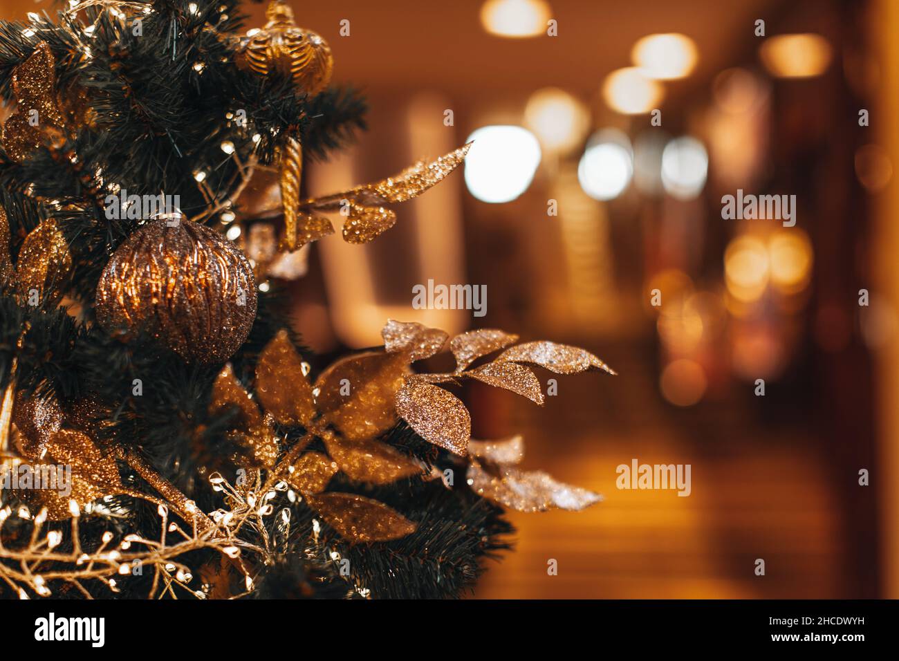 A branch of the Christmas tree decorated with a golden plant leaves, Christmas ball and garlands light. New Year composition in a festive interior Stock Photo