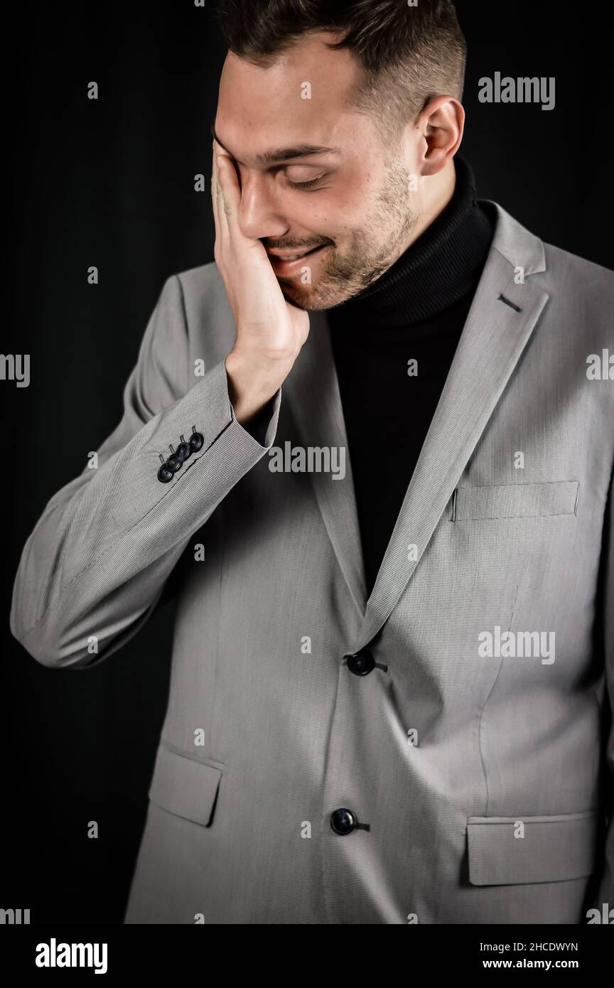 portrait of a young businessman in a gray suit who is extremely tired rubs his face trying to recover Stock Photo