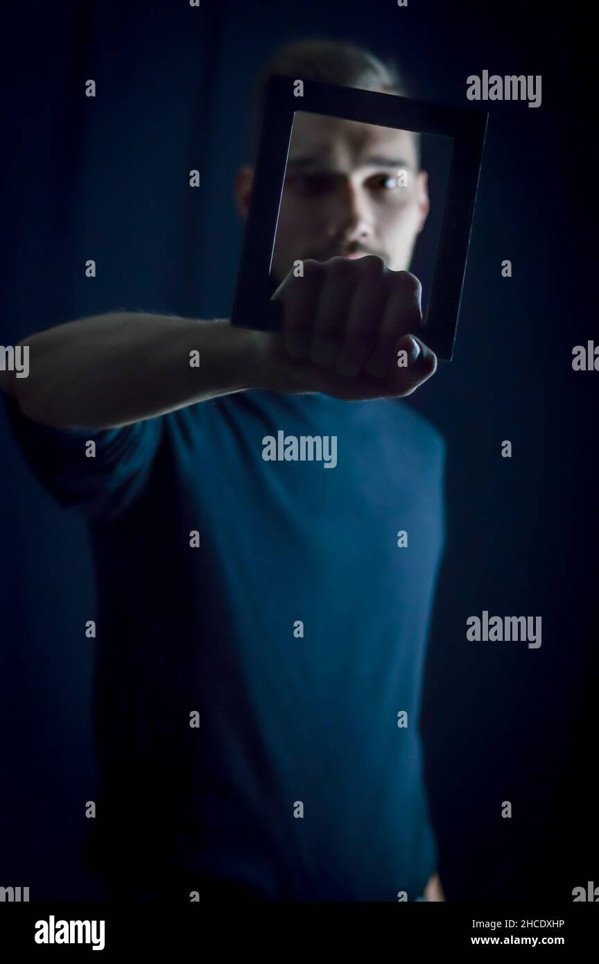 portrait of a young man holding a frame in front of his face, concept ...