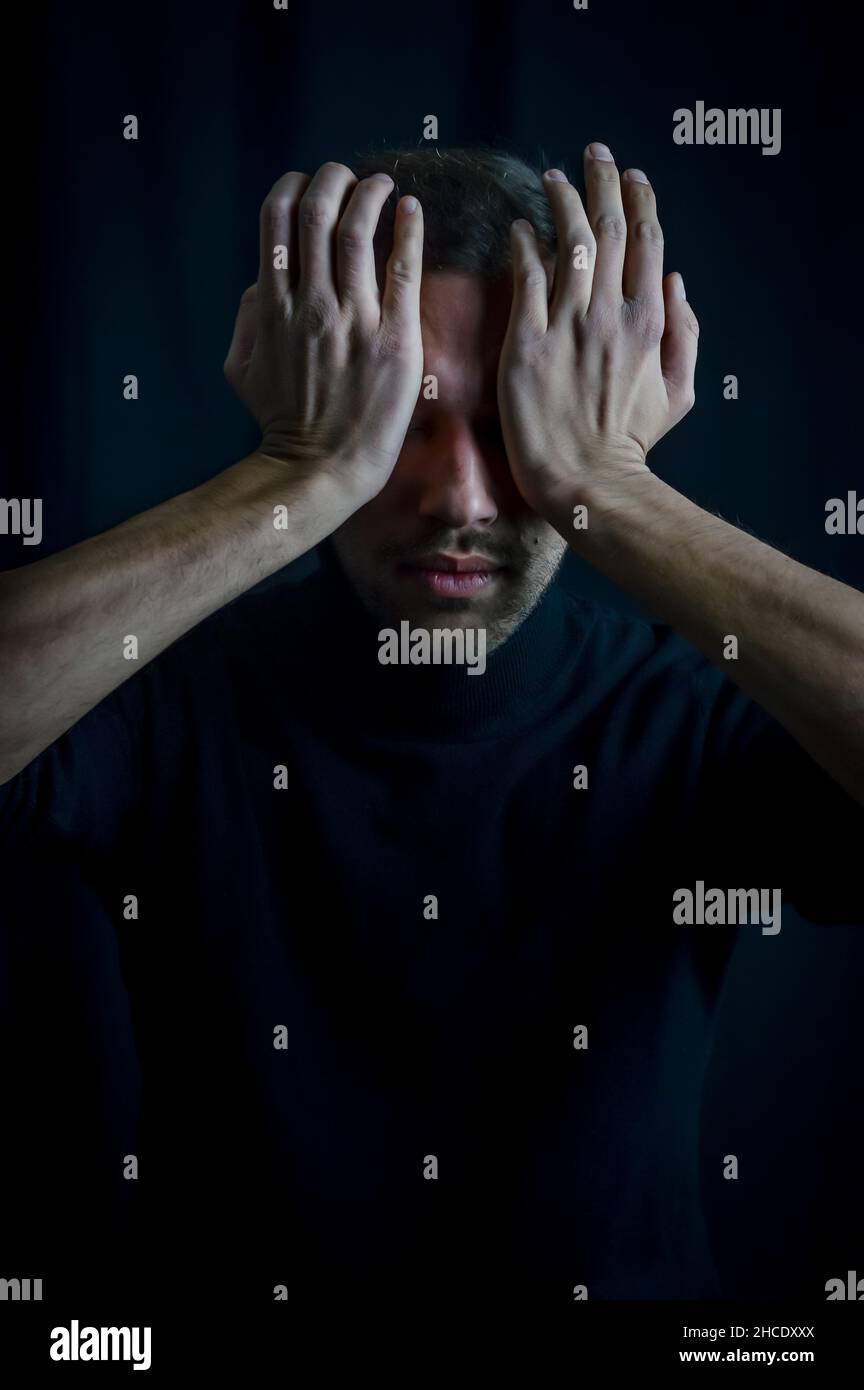 portrait of a young man covering his eyes with his palms so as not to ...