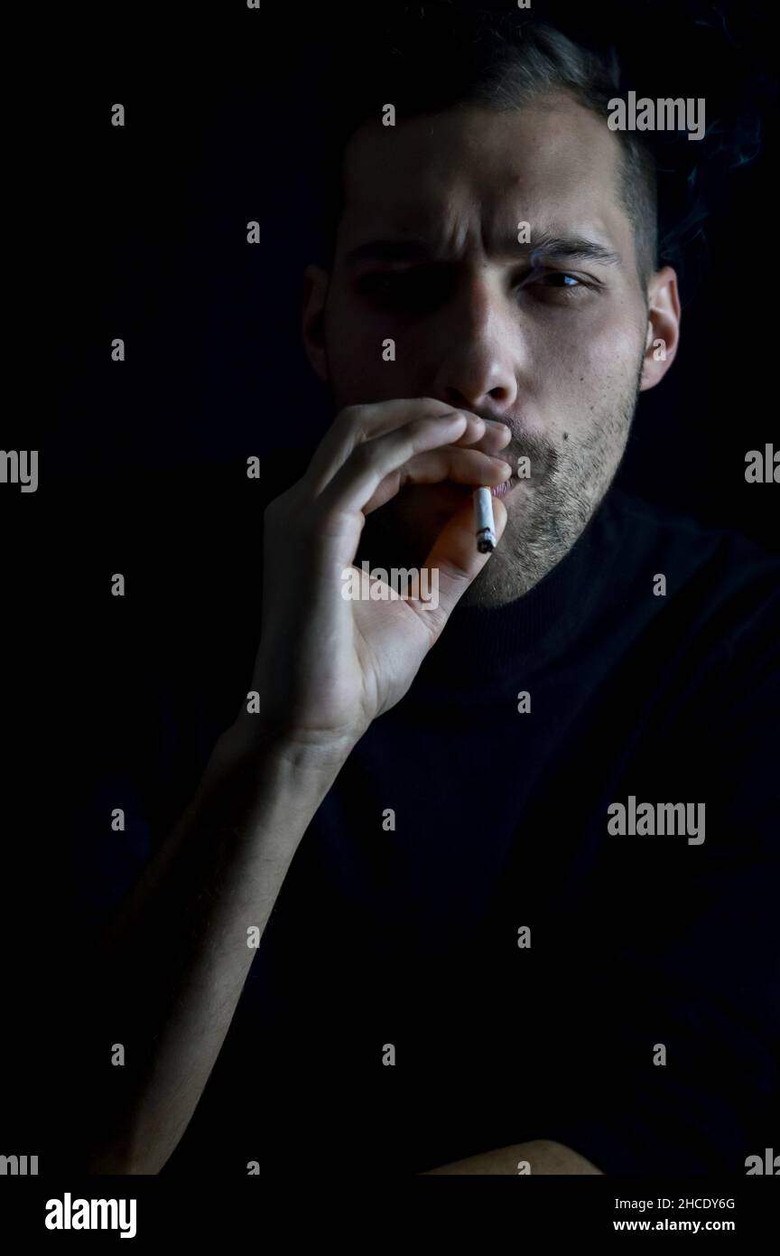 portrait of a young man who is inhaling the smoke of a cigarette while ...