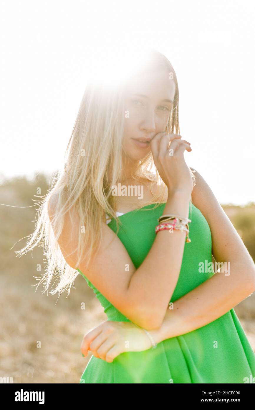 Pensive blond teen in a green dress on a beach. Backlit sun shines on her hair Stock Photo