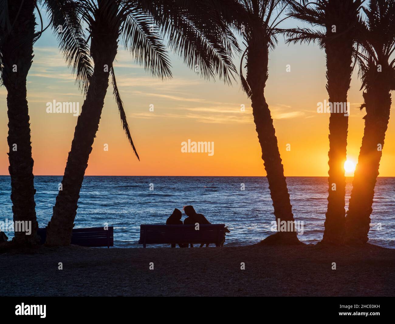 Silhouette of a couple with a dog on the sandy shore of Almuñecar beach at sunset. Stock Photo