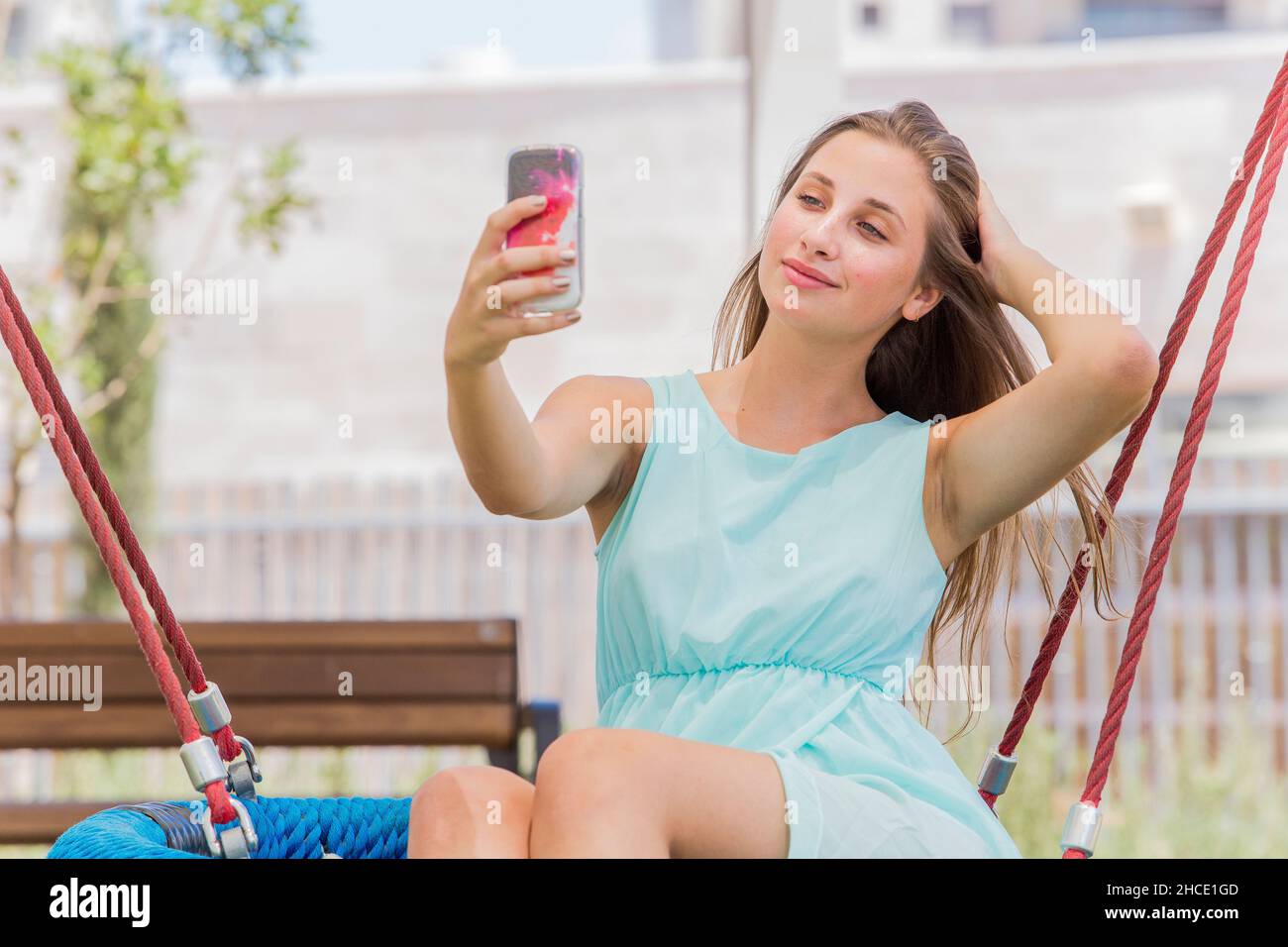 Beautiful blonde teen takes a picture of herself with her mobile phone in the park Stock Photo
