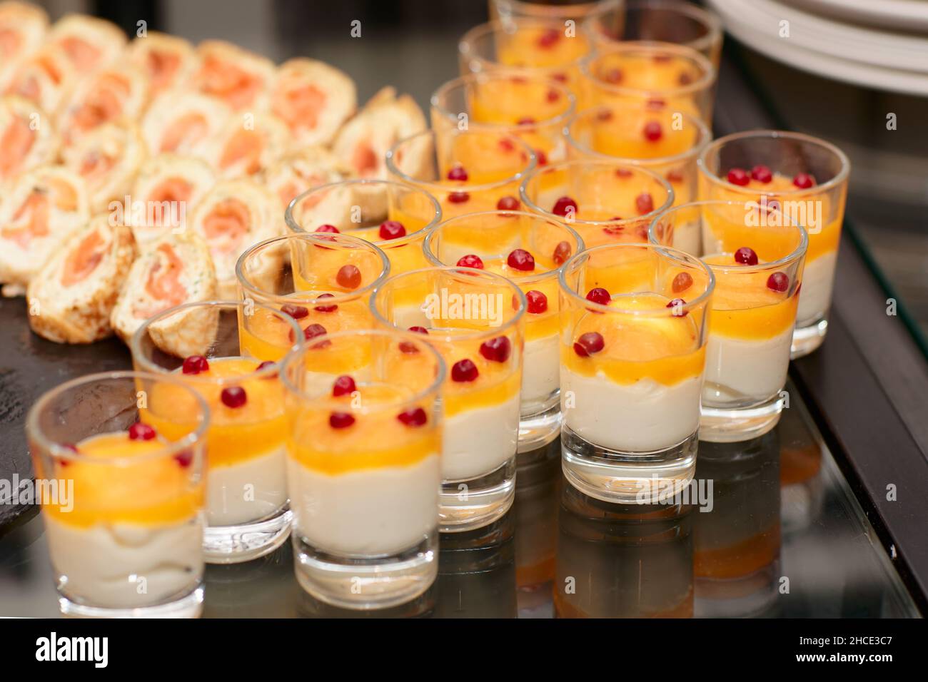 Glasses of panna cotta and pancake rolls with salmon on banquet table Stock Photo