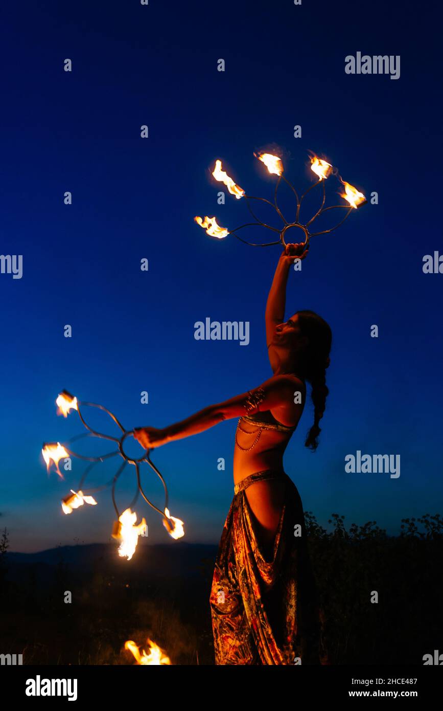 Side view of talented female fire dancer in costume standing with