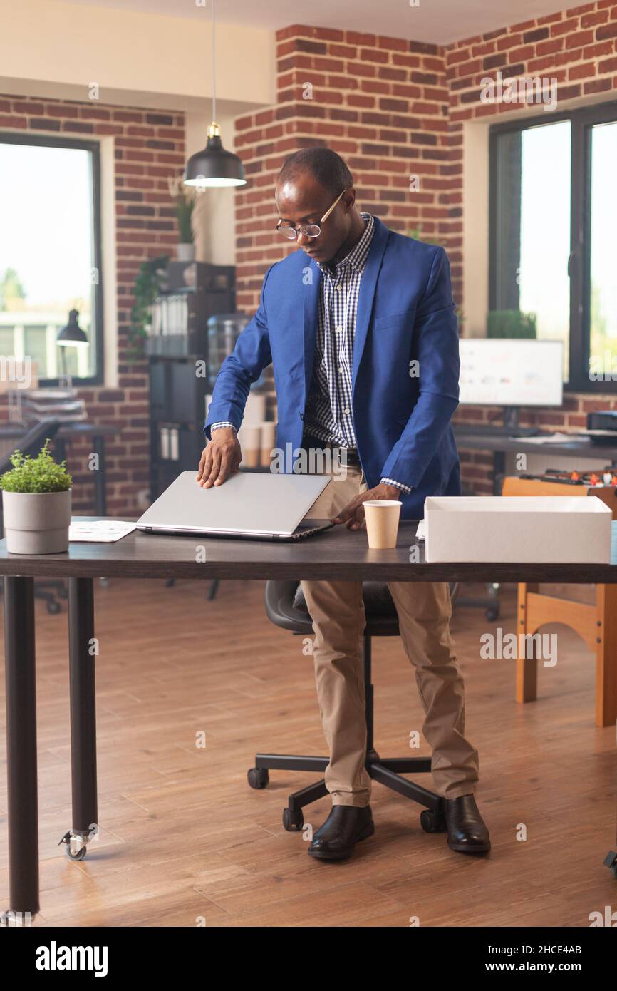 African american person gathering things in box after getting fired from business job. Frustrated person preparing to leave work after being discharged and dismissed by manager. Stock Photo