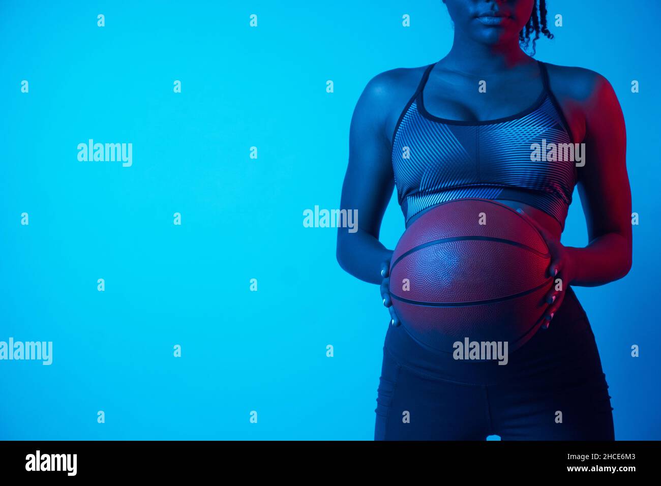 Confident African American female athlete holding basketball in blue light Stock Photo