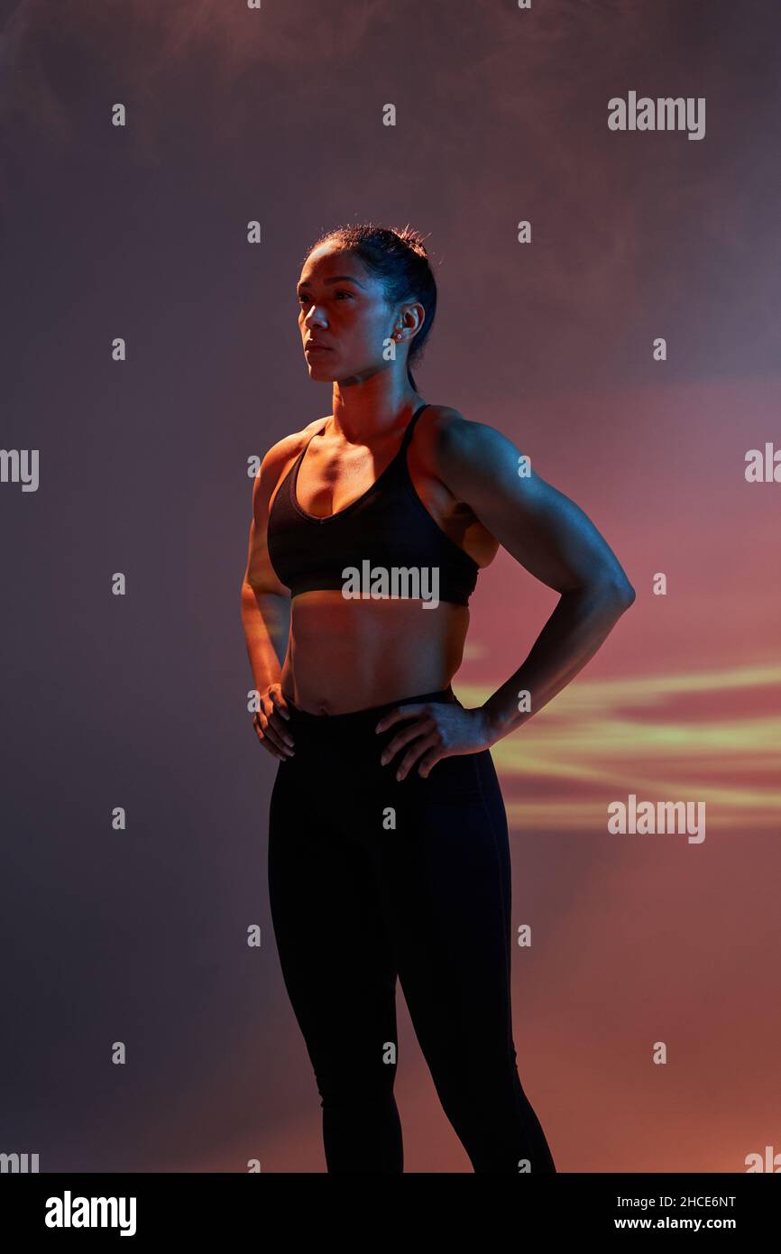 Confident slim female athlete in sportswear standing with hands on hips ...