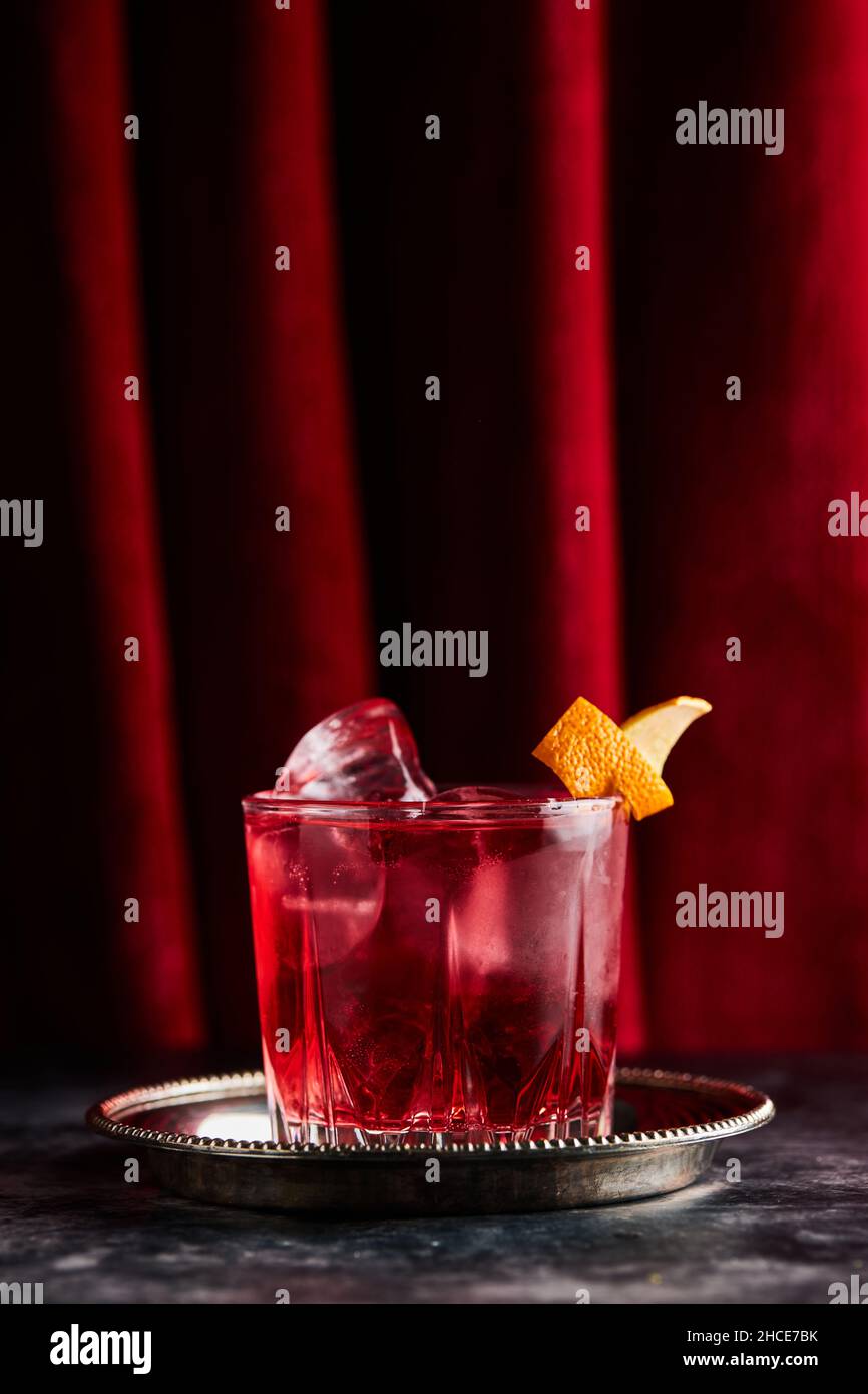 Glass of refreshing Negroni cocktail with bitter flavor and ice garnished with orange peel and