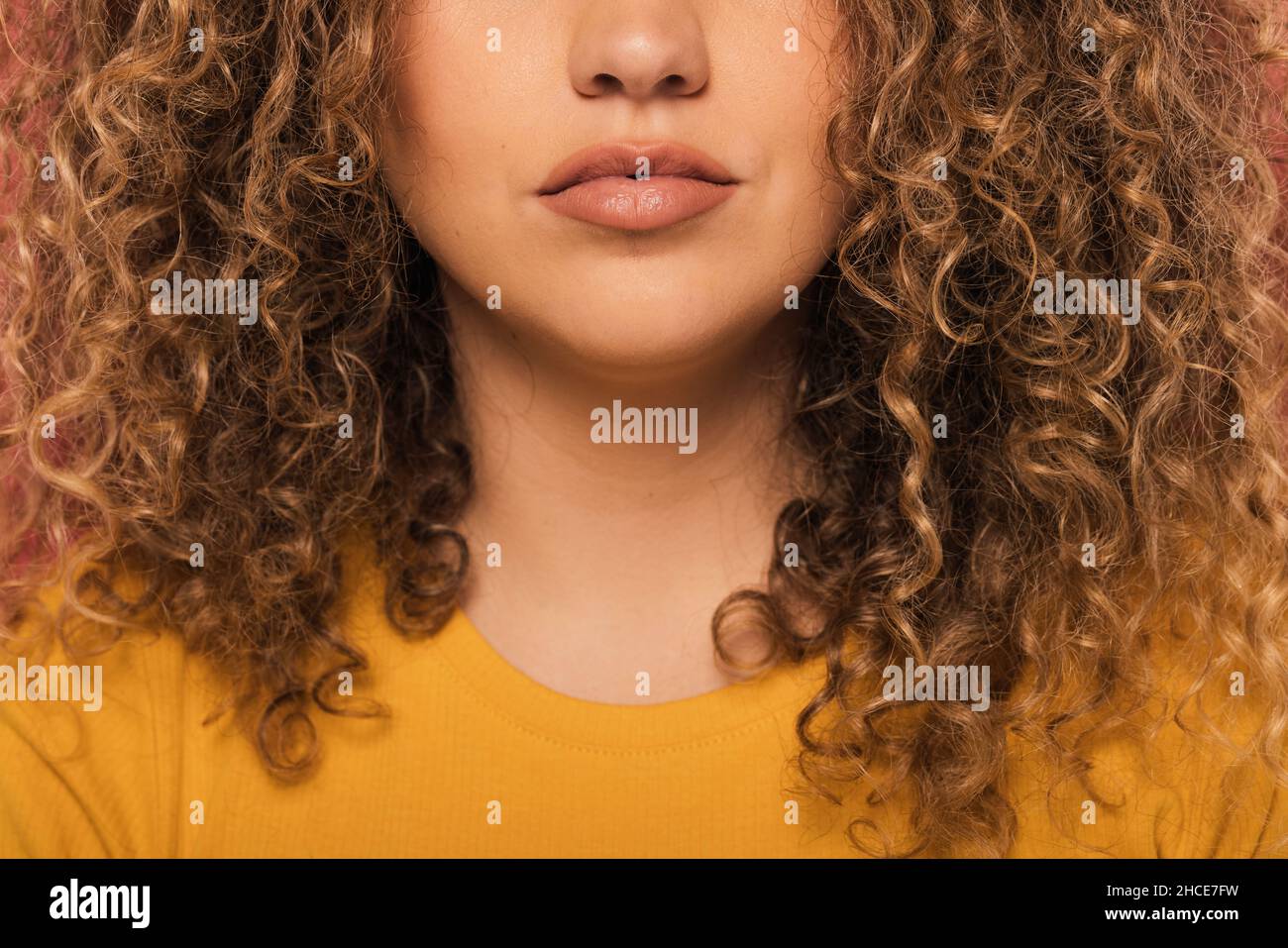 Crop unrecognizable Woman portrait with curly hair looking at camera while standing on pink background Stock Photo