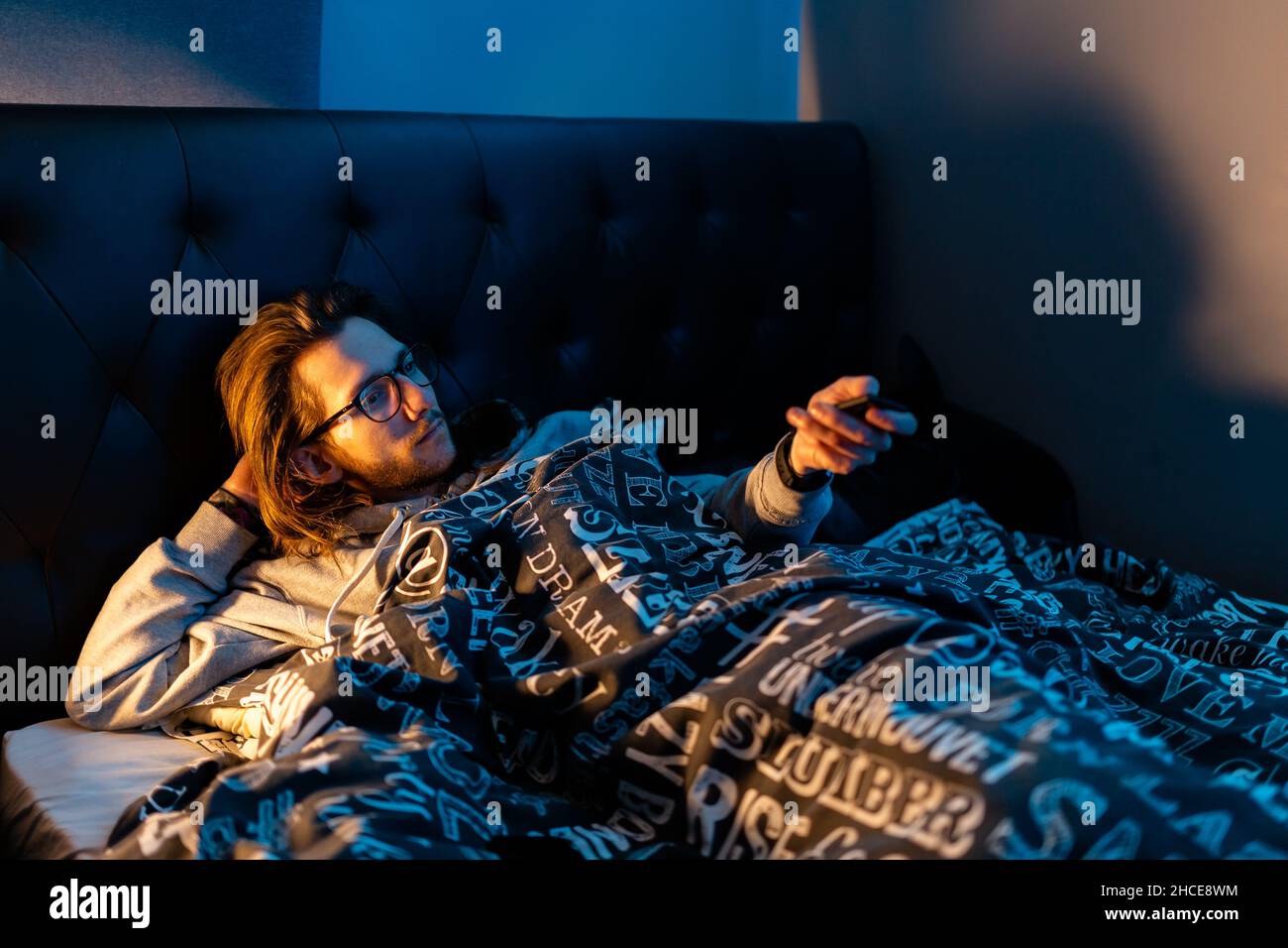 A young man laying in bed watching TV before he goes to sleep. Life style, after dark concept Stock Photo