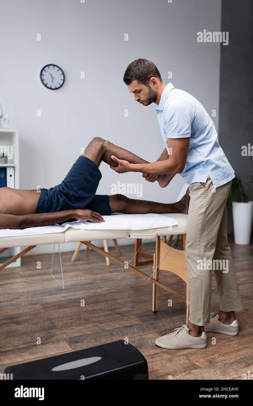 physical therapist massaging leg of african american man in rehab clinic Stock Photo