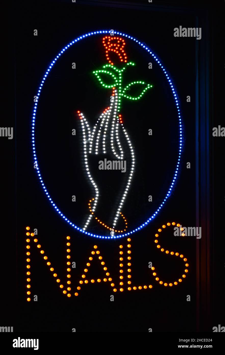 A neon sign in the window at a nail bar, showing a hand holding a rose. Stock Photo