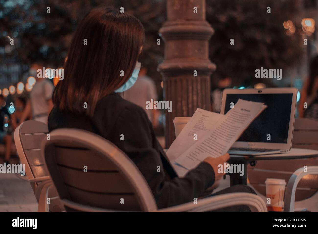 Young black-haired female manager with a mask reviewing company contracts in a coffee shop Stock Photo