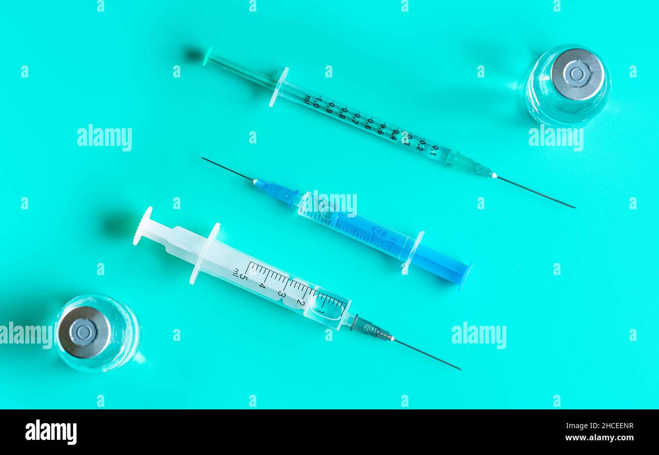 Hypodermic syringes and needles with vaccine bottles on cyan table
