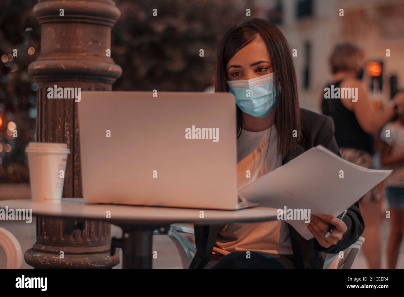Business woman with mask concentrated on her work sitting in the city cafeteria drinking coffee with her laptop Stock Photo