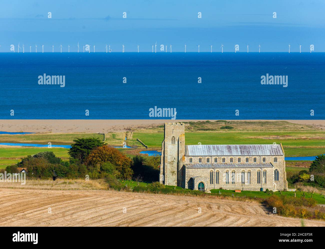 View of Salthouse showing the village Church of St Nicholas, grazing marshes and shingle bank, with the 'Sheringham Shoal' offshore windfarm in distan Stock Photo