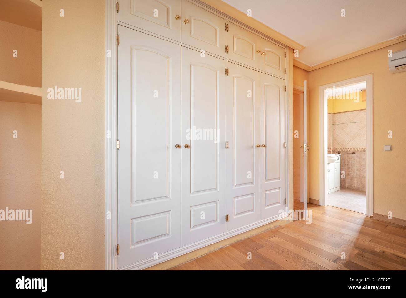 Bedroom with white walk-in closet and en-suite bathroom with parquet flooring Stock Photo