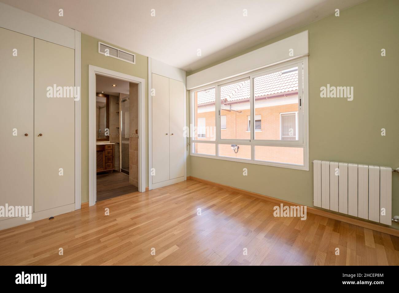 Empty room with greens, en-suite bathroom and oak floors with large windows. Stock Photo