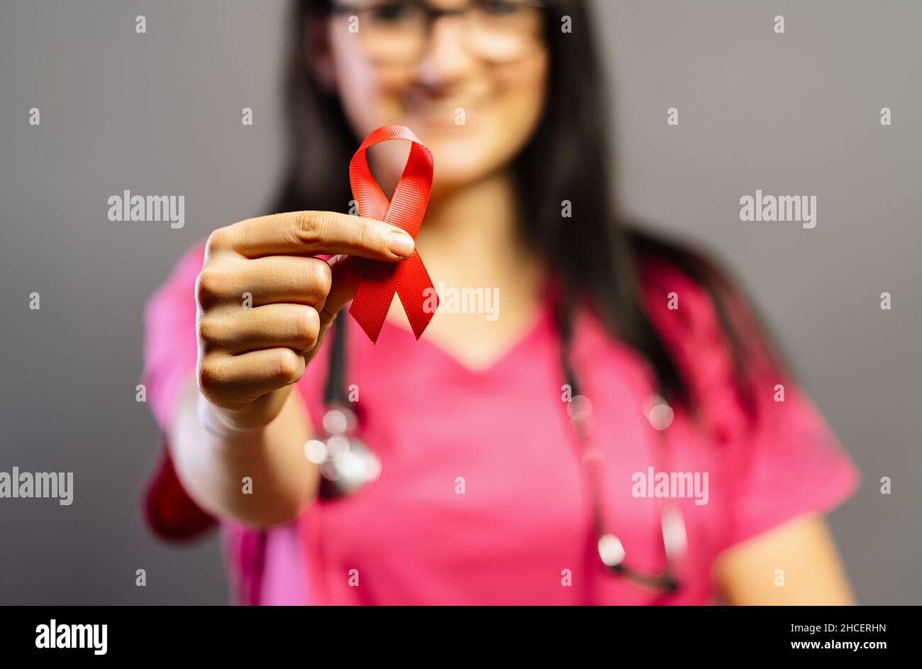 Doctor holds red badge ribbon in hands to support AIDS Day. Healthcare, medicine and AIDS awareness concept. Stock Photo