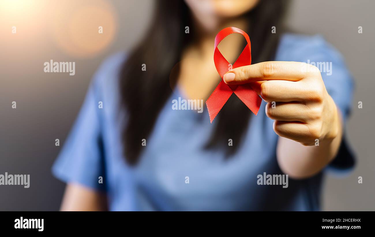 Doctor holds red badge ribbon in hands to support AIDS Day. Healthcare, medicine and AIDS awareness concept. Stock Photo