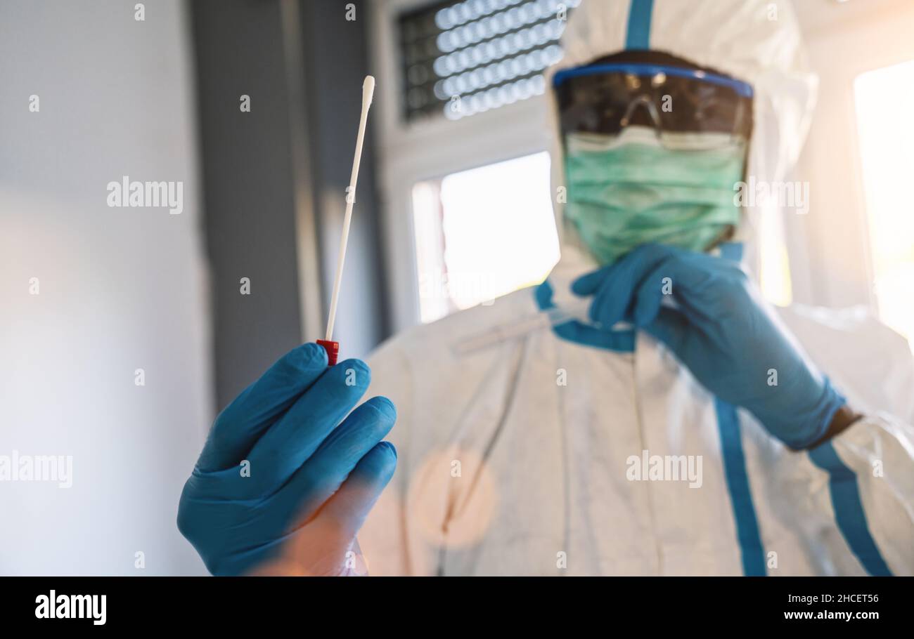 Medical healthcare technologist holding COVID-19 swab collection kit, wearing white PPE protective suit mask gloves, test tube for taking OP NP patien Stock Photo