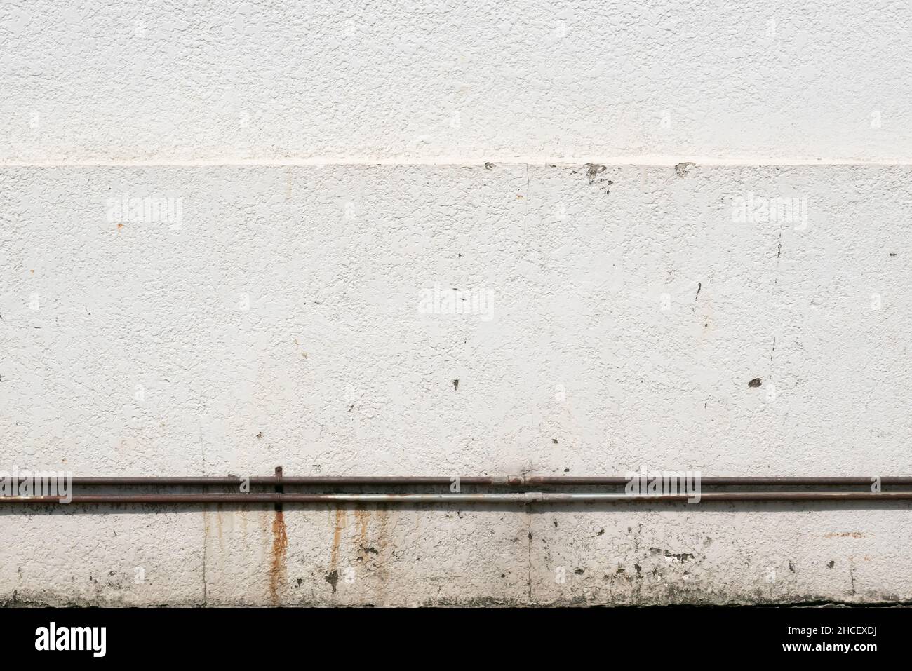 White stucco wall with rusty metal pipe background Stock Photo