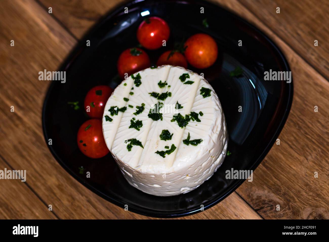 Tasty white cheese with spices and cherry tomatoes on cutting board Stock Photo
