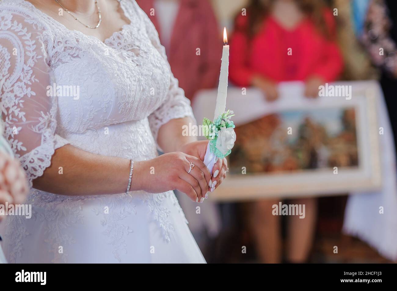 The bride and groom hold shining candles during the ceremony in the church. Hands of newlyweds with candles in the church. Church religious details Stock Photo