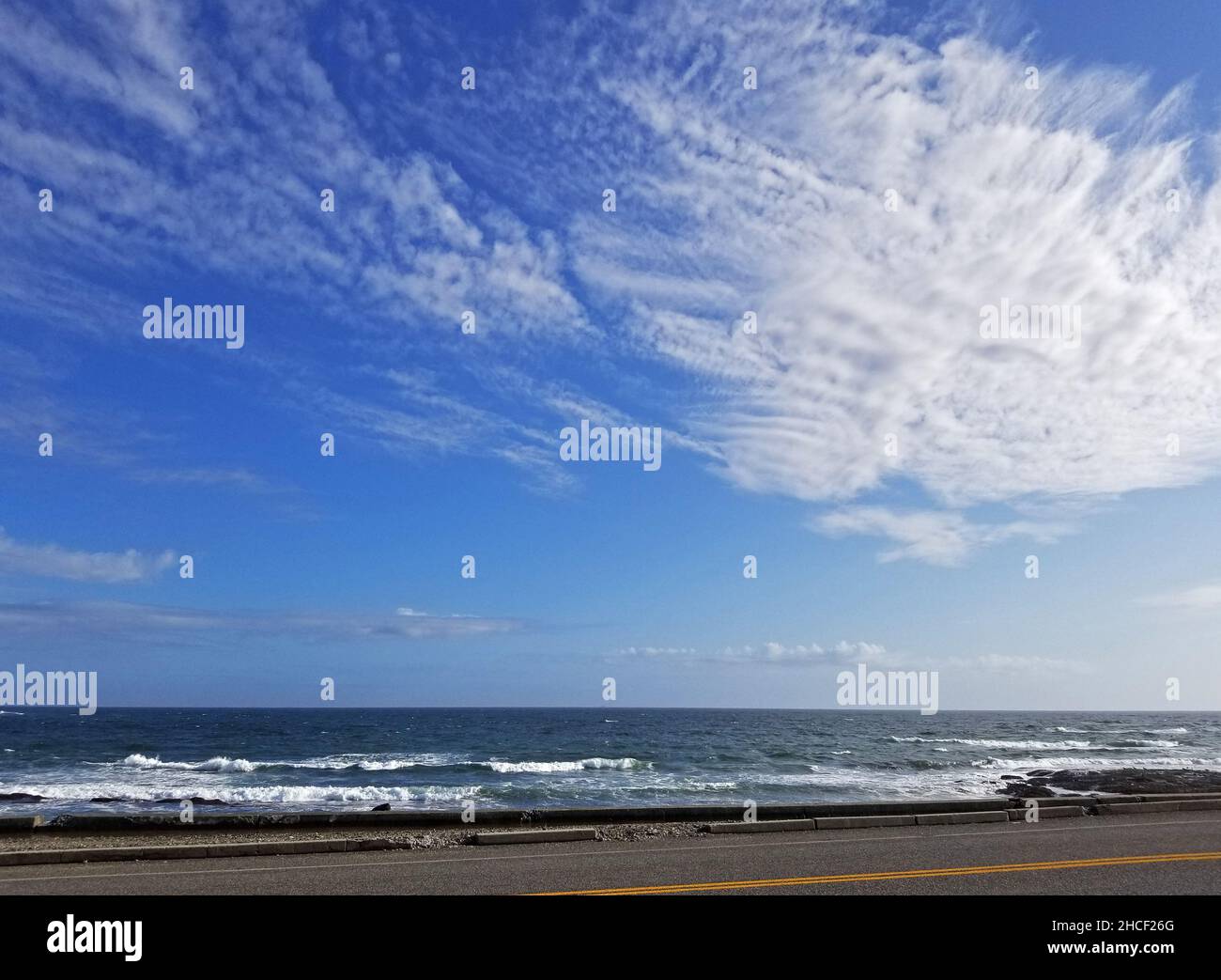 Ocean waves crash into rocky shore at Brenton Point in Newport, Rhode Island, while some stratus clouds drift by on an otherwise blue sky -05 Stock Photo