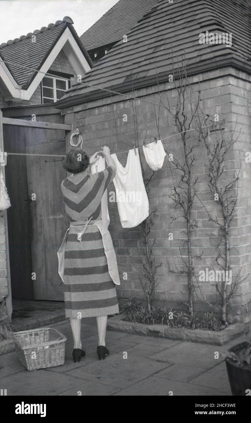1950s, historical, a lady standing outside a house on a patio hanging up  some washed clothes on a clothesline to dry, England, UK. In this decade,  clotheslines or washing lines were the